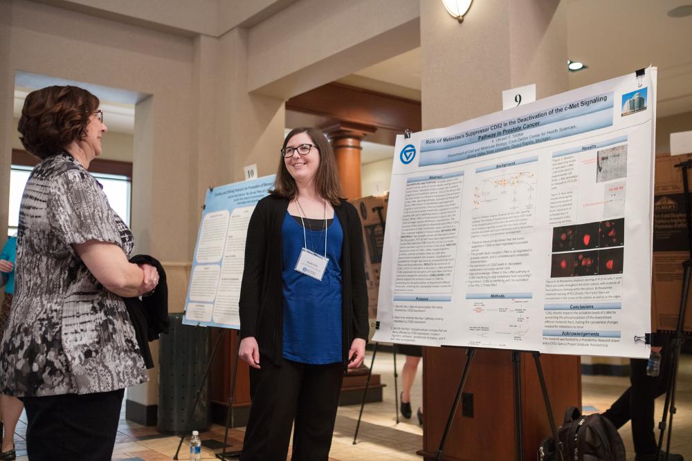 Student smiling as she presents her poster to a smiling onlooker